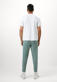 Bílý krátký rukáv tričko v kombinaci s mátově zelenými zúženými tepláky. Tričko má kulatý výstřih; tepláky mají elastické manžety a minimální švy.