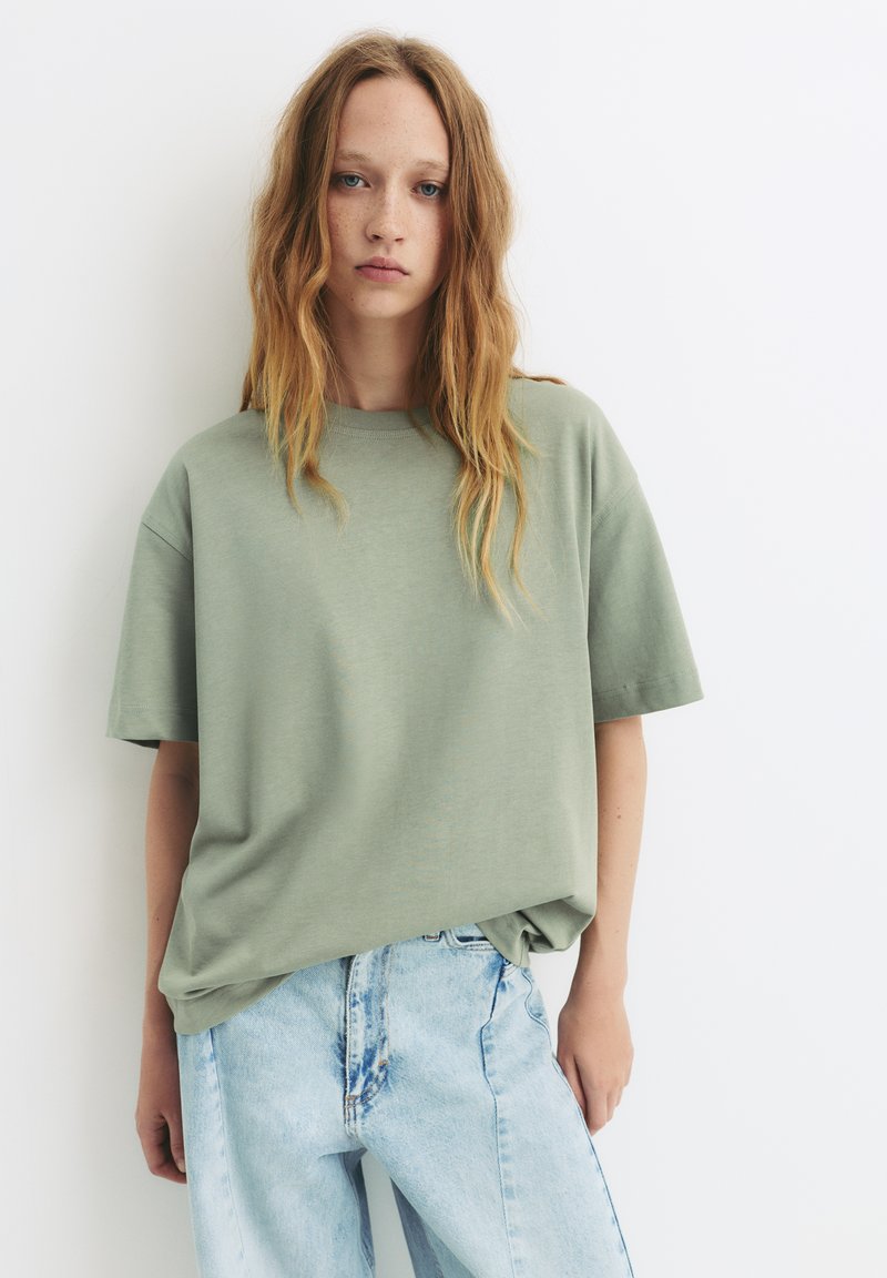 Groene katoenen t-shirt met een relaxte fit, korte mouwen en een ronde hals, gecombineerd met lichtblauwe versleten denim jeans.
