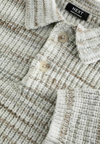 Strikket sweater i lysegrå med brune accenter. Har en kravehalsudskæring og to klare knapper, tekstureret med et ribbet mønster.