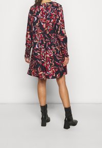 Schwarzes langärmeliges Kleid mit buntem Blumenmuster, gerafftem Taillenbereich und ausgestelltem Rock. Kombiniert mit schwarzen, hohen Stiefeletten.