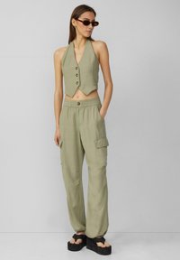 Oliwkowy dwuczęściowy strój składający się z bezrękawkowego, zapinanego na guziki, krótkiego topu oraz spodni cargo z elastycznym pasem i kieszeniami bocznymi. Masywne platformy sandały.