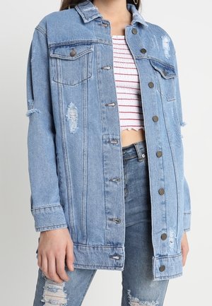 Woman wearing light blue distressed denim jacket over a white cropped top with red stripes, paired with ripped blue jeans.