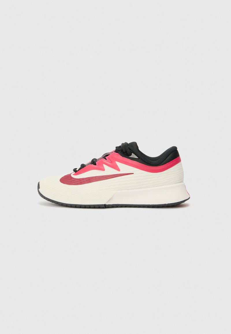 Sapatilha de corrida com parte superior em creme, detalhes em vermelho e preto, e superfície texturizada. Apresenta atacadores pretos e uma sola almofadada para conforto.