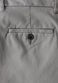 Tissu gris avec un motif tissé texturé, comportant une poche rectangulaire et un bouton noir au centre.