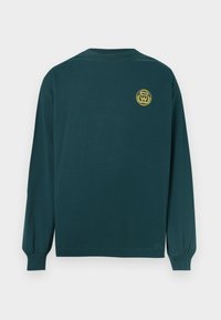 Long-sleeve shirt in dark green cotton with a round neckline, featuring a yellow emblem on the upper back. Simple, relaxed fit.