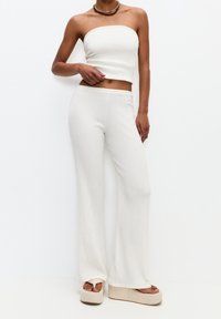 Femme portant un crop top sans manches à rayures blanches, un pantalon large taille haute assorti, des sandales à plateforme et un collier ras du cou sur fond blanc.