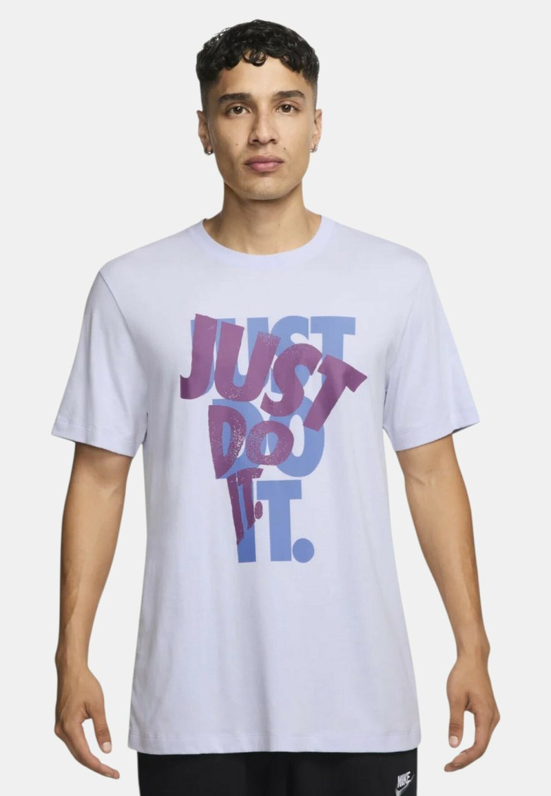 Camiseta de manga corta blanca con texto atrevido y multicolor que dice "SIMPLEMENTE HAZLO". Los colores del texto incluyen púrpura y azul.