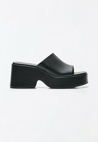 Sandale mule à plateforme noire avec orteils ouverts et semelle épaisse incurvée sur fond blanc.