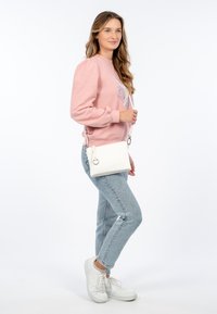 Sudadera rosa con mangas abullonadas, diseño gráfico; jeans de mezclilla clara; bolso bandolera blanco con cremallera y detalle de anillo; zapatillas blancas.