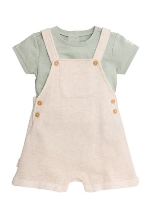 Peto corto beige suave con botones de madera, llevado sobre una camiseta de bebé de manga corta color verde claro con un botón de presión en el escote.