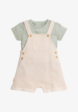 Peto corto beige suave con botones de madera, llevado sobre una camiseta de bebé de manga corta color verde claro con un botón de presión en el escote.