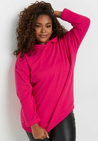 Sudadera fucsia hecha de una tela suave, con un corte holgado, mangas largas y un dobladillo asimétrico. Presenta un cuello con cordón para ajuste.