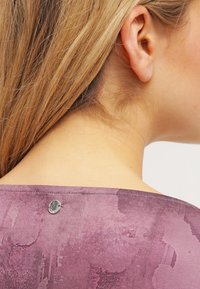 Top morado con estampado que presenta un escote redondeado y un pequeño detalle metálico en la parte trasera, con una textura suave y una tela delicada.