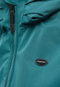 Blauwgroene jas met een gestructureerd zigzagpatroon, zwarte ritssluiting en een klein zwart logo op de borst.