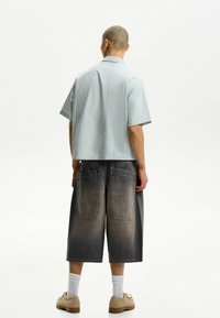 Kortærmet, lyseblå stribet skjorte parret med mørkegrå denimshorts til knæet. Teksturstof og to baglommer synlige.