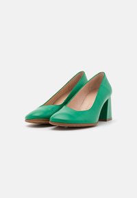 Chaussures à talons hauts en cuir vert avec un bout pointu et un talon large. L'intérieur présente une doublure lisse et neutre.