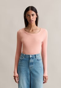 Haut à manches longues en rib, de couleur pêche douce, avec un décolleté arrondi et des poignets à volants, associé à un jean en denim bleu clair taille haute.
