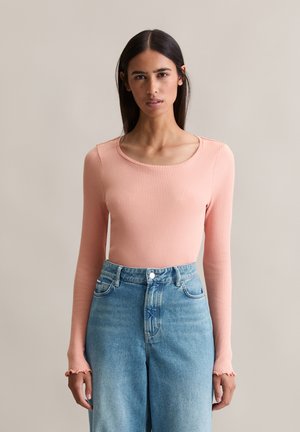 Long-sleeve ribbed top in soft peach, featuring a scooped neckline and frilled cuffs, paired with high-waisted light blue denim jeans.
