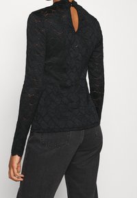 Sort langærmet top lavet af struktureret blonde, med høj halsudskæring og detaljer med nøglehul på ryggen, i en tætsiddende silhuet.