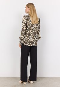 Floral blouse in cream, featuring green and blue patterns, gathered shoulders, and long sleeves, paired with black wide-leg pants and heeled sandals.