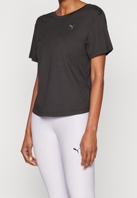 Svart T-shirt med korta ärmar tillverkad av mjukt tyg med rund halsringning och en liten grå Puma-logotyp på bröstet, kombinerad med ljusgrå leggings.