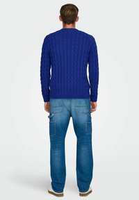 Blå kabelstrikket sweater med lange ærmer og ribbet kant. Kombineret med lyseblå jeans med flere lommer og en afslappet pasform.