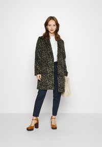 Leparda raksta mētelis, garas piedurknes, atvērta priekšpuse, saskaņots ar baltu kreklu un tumši ziliem biksēm. Koka bloka papēža apavi. Beigēna rokassoma.