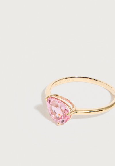 Λεπτό χρυσό δαχτυλίδι με τριγωνική ροζ πολύτιμη πέτρα στερεωμένη σε τριπλή στήριξη, φωτογραφημένο σε λευκή επιφάνεια.