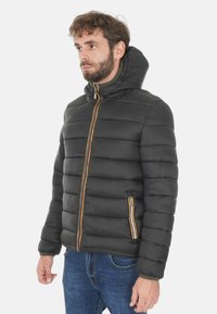 Giacca a vento nera con cuciture orizzontali, chiusura con zip, dettagli a strisce gialle, rosse e bianche vivaci sulla zip, e cappuccio.