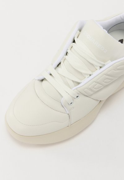 Sneaker en cuir blanc avec un bout arrondi, des lacets plats et un col rembourré. Présente un logo en relief et une semelle en caoutchouc blanc. Texture lisse.