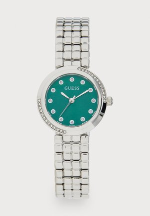 Srebrny metalowy bransoletowy zegarek z niebieską tarczą, kryształowymi znacznikami godzin, kryształowymi akcentami na bezel oraz logo Guess na godzinie 12.