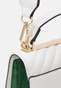 Valkoinen nahkalaukku, jossa on kultaiset metalliosat ja vihreä matelijaeläin-kuvioitu yksityiskohta. Suunnittelussa on tikattu kuviointi ja kontrastiväriset reunat.