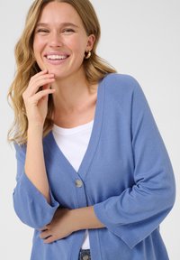 Cardigan bleu clair avec un col en V, fermeture par bouton et manches trois-quarts. Texture en tricot doux et détails en côtes le long de l'ourlet.