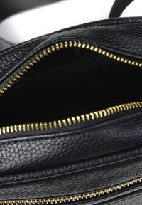 Interno di una borsa in pelle nera con finitura testurizzata, caratterizzato da dettagli in zip dorati. Parte superiore aperta con una tasca zippata visibile all'interno.