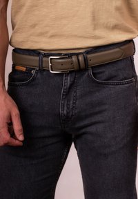 Olive green leather belt with a silver metal buckle, featuring a textured finish and multiple adjustment holes, worn with dark denim jeans.