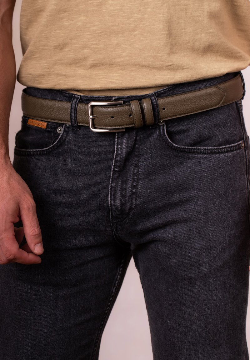 Olive green leather belt with a silver metal buckle, featuring a textured finish and multiple adjustment holes, worn with dark denim jeans.
