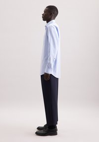 Camicia button-up a quadri blu chiaro con maniche lunghe, abbinata a pantaloni blu scuri e scarpe nere. Il design presenta un colletto classico.