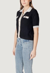 Cardigan nero lavorato a maglia con colletto bianco, maniche corte e dettagli con bottoni. Presenta un tessuto testurizzato e tasche frontali.
