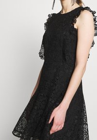 Musta pitsimekko, jossa on tiukka yläosa ja levenevä hame. Varustettu röyhelöpitsireunuksilla olkapäillä ja monimutkaisilla kukkakuosisilla yksityiskohdilla.