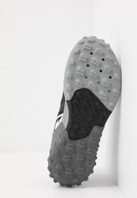 Zool van een zwart en grijs sportbroek met een robuuste, gestructureerde looprand, ontworpen voor buiten- of trailgebruik.