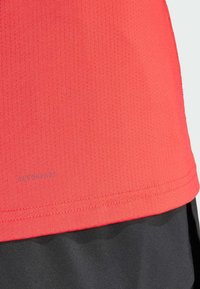 Red athletic shirt featuring a textured, moisture-wicking fabric with small perforations. "AEROREADY" branding is visible near the hem.