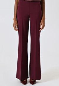 Pantalon à jambes larges en tissu bordeaux profond à la texture lisse ; design taille haute associé à des escarpins bordeaux brillants à bouts pointus.