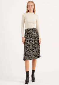 Lange mouw, geribbelde crèmekleurige top gecombineerd met een zwarte midi-rok met bloemen, voorzien van kleine witte en oranje bloemen. Model draagt zwarte enkellaarsjes.