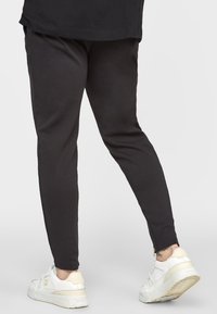 Mustat kapealahkeiset collegehousut, valmistettu puuvillasekoitteesta, joissa on sileä pinta ja nilkassa vetoketjuyksityiskohta, yhdistetty valkoisiin lenkkareihin.