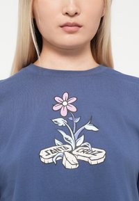 T-shirt in cotone blu con una grafica floreale che presenta un fiore rosa e foglie verdi, inserita in un design con la scritta "SANTA CRUZ."