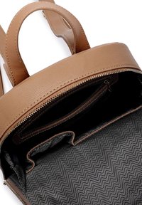 Hnědý kožený batoh s dvěma horními rukojeťmi, zipovým uzávěrem a černým interiérem s cik-cak vzorem. Obsahuje vnitřní kapsu.