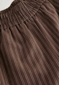 Tissu rayé brun avec une taille élastique froncée. Présente de fines rayures blanches contrastantes courant verticalement sur le matériau.