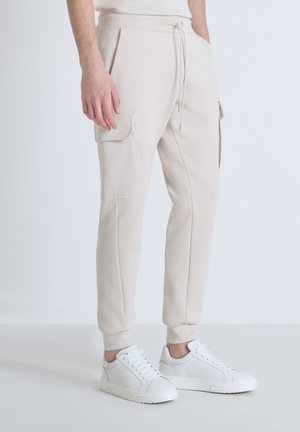Beige joggerbroeken van zachte stof, met zijzakken, een koordsluiting bij de taille en taps toelopende pijpen. Gecombineerd met witte sneakers.