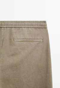 Khaki bavlněné kalhoty s elastickým pasem, které mají jedno zadní našité kapsu s prošívaným okrajem. Hladká textura a neformální design.
