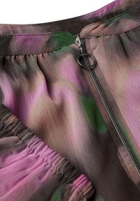 Multifarvet stoftop med smocket kant, der har nuancer af pink, grøn og brun; inkluderer en sølv lynlås og en blød tekstur.